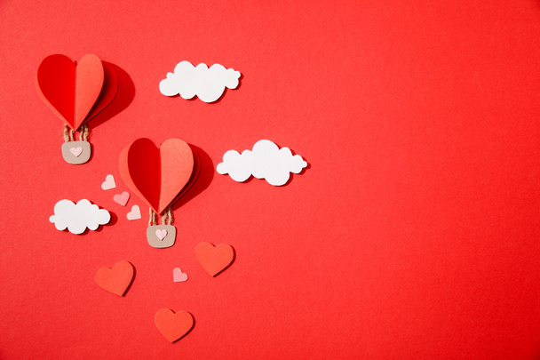 top view of paper heart shaped air balloons in clouds on red background - Фото, зображення