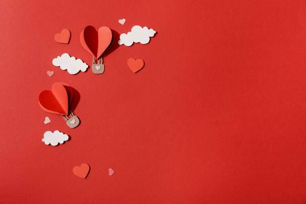 top view of paper heart shaped air balloons in clouds on red background - Fotó, kép
