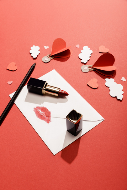 paper clouds and heart shaped air balloons, envelope with lip print, lipstick and pencil on red background - Foto, Imagem