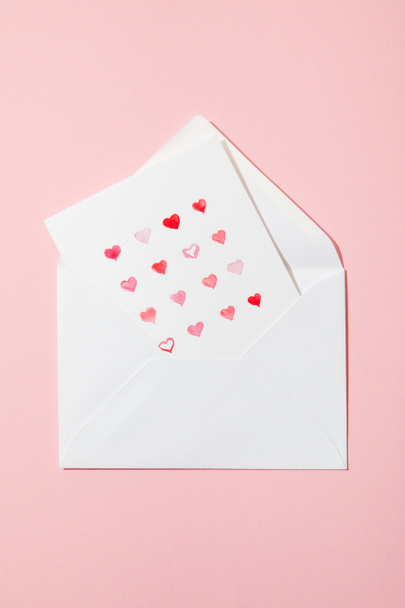 top view of greeting card with hearts in white envelope isolated on pink - Fotografie, Obrázek