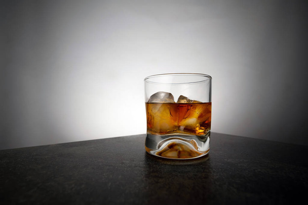 Glass of aged golden whiskey with ice cubes on the table. Amber colored alcohol beverage with rocks at the bar - 写真・画像