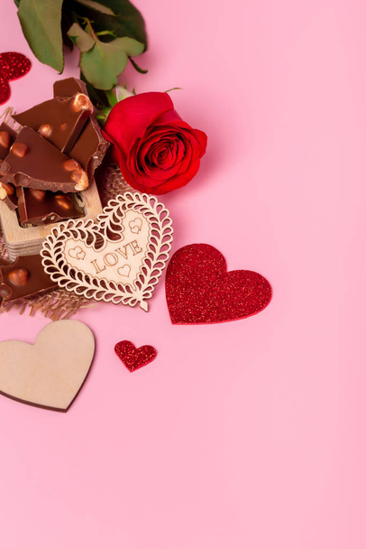 День святого Валентина з червоними серцями, шоколадними цукерками, молочним шоколадом і червоною трояндою на рожевому тлі. Романтична атмосфера і любовні символи. - Фото, зображення