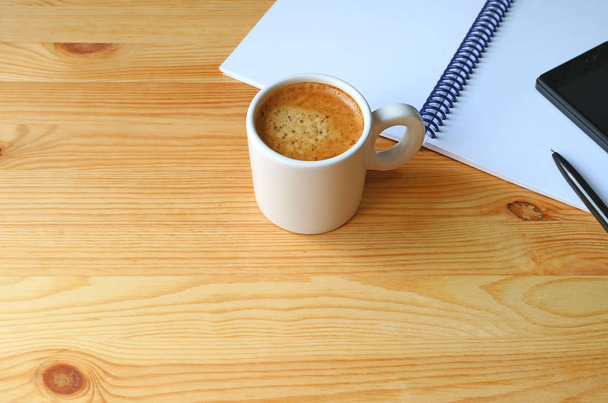 Κύπελλο ζεστό καφέ με ένα σημειωματάριο και κινητό τηλέφωνο σε ξύλινο γραφείο εργασίας, δωρεάν χώρο για το σχεδιασμό - Φωτογραφία, εικόνα