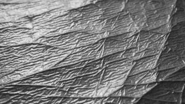 Stříbrný zmačkaný povrch ošuntělého obalového materiálu s vráskami a záhyby. Abstraktní lesklé černé a bílé pozadí - Záběry, video