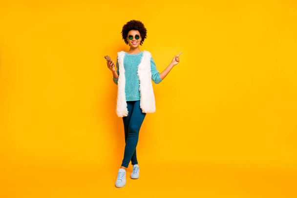 Full size photo positive afro american girl use smartphone browse promo point finger copyspace wear blue pants trousers teal jumper white vest stylish trendy isolated yellow color background - Foto, Bild