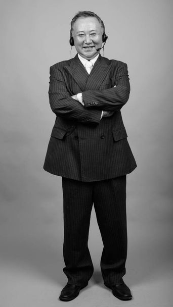 Студийный снимок зрелого азиатского бизнесмена в качестве представителя колл-центра на сером фоне в черно-белом - Фото, изображение