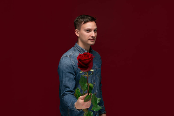 Νεαρέ όμορφε άντρα που κρατάς ένα κόκκινο τριαντάφυλλο για να δώσεις στην αγαπημένη σου. - Φωτογραφία, εικόνα