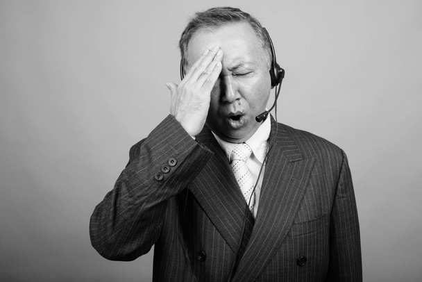 Studio laukaus kypsä aasialainen liikemies kuin call center edustaja vastaan harmaa tausta mustavalkoinen - Valokuva, kuva