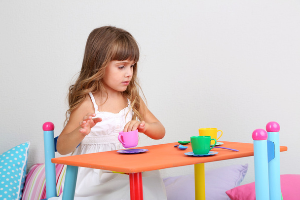 Little girl draws sitting at table in room on grey wall background - Foto, immagini