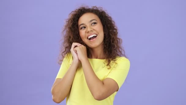 Beautiful happy african young woman in yellow t-shirt smiling and enjoying of something over purple background isolated - Felvétel, videó
