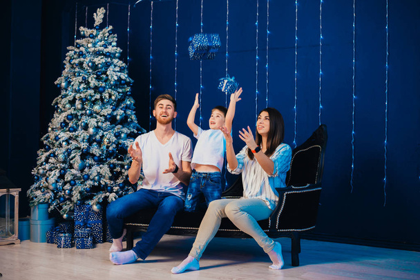 happy young family with adorable little son sitting together with presents near christmas tree    - Foto, imagen
