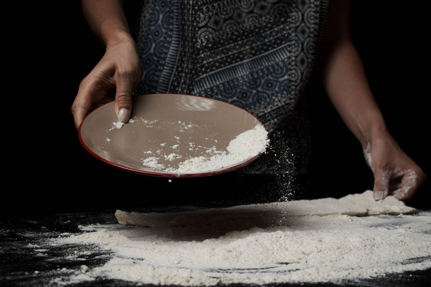 mid section of woman sifting flour and preparing dough on black background - Foto, Bild
