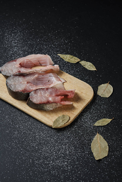 close-up view of fish slices with bay leaves on wooden board on black background   - Foto, Bild