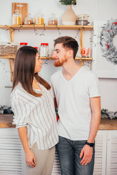 beautiful happy young couple smiling each other in kitchen at christmastime - Photo, image