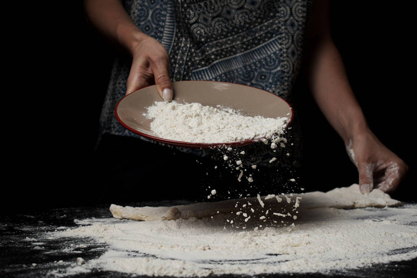 mid section of woman sifting flour and cooking dough on black background - Foto, Bild