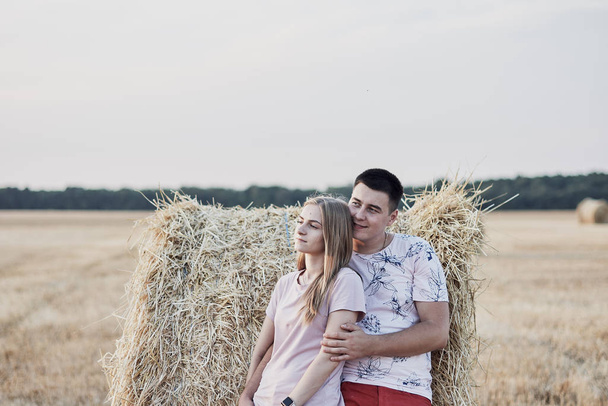 happy young couple near hay bales in beautiful field during harvest - Foto, afbeelding