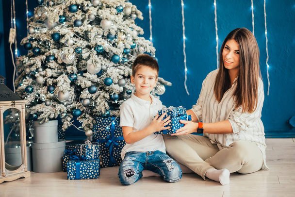 happy young mother with adorable little son together near christmas tree with gift boxes - Foto, Bild