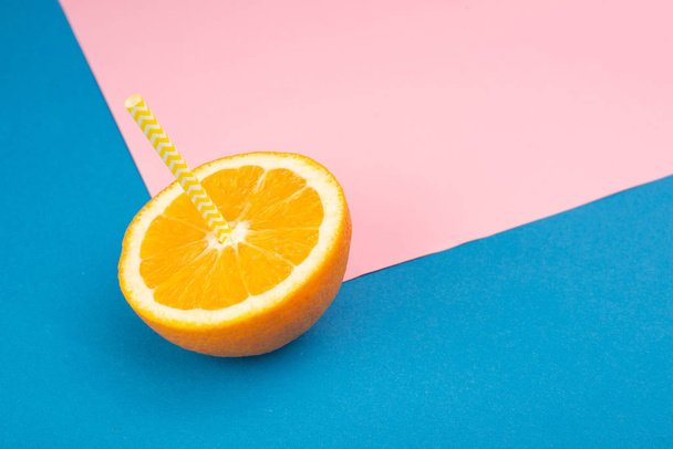 close-up view of sliced orange with straw on blue and pink background - Foto, Bild