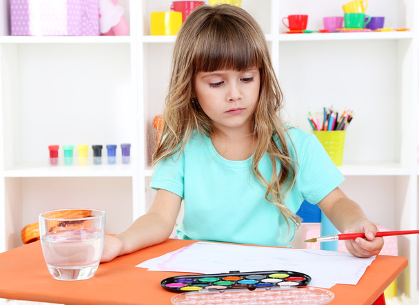 holčička kreslí sezení u stolu v pokoji na pozadí police - Fotografie, Obrázek