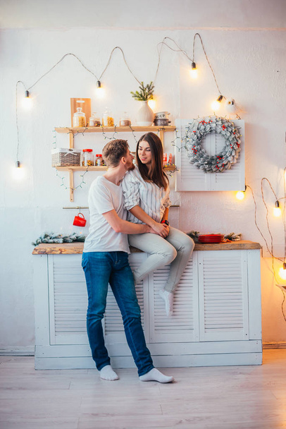 beautiful happy young couple smiling each other in kitchen at christmastime - Foto, imagen