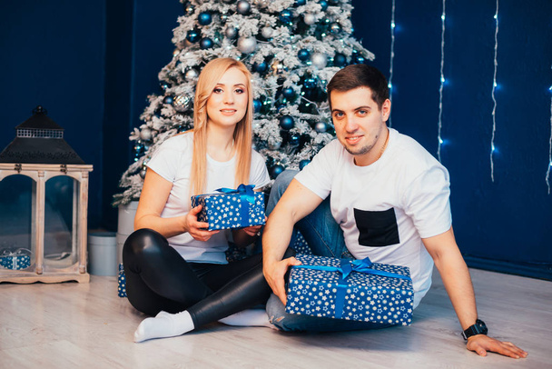 feliz joven pareja con regalos sentado juntos cerca de árbol de Navidad
 - Foto, imagen