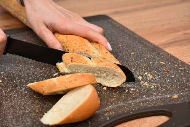 cropped shot of woman cutting fresh bread with knife on wooden table   - 写真・画像