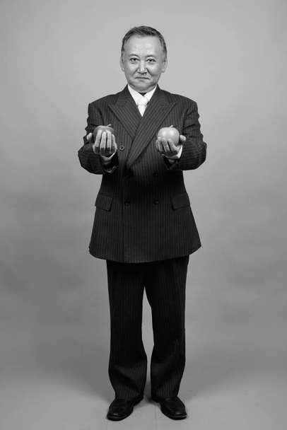 Studio shot of mature Asian businessman holding apple against gray background in black and white - Foto, Imagen
