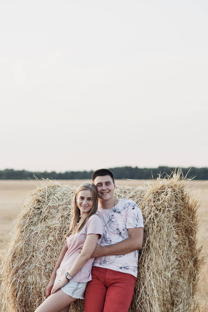 beautiful happy young couple near hay bales in field during harvest - Фото, зображення