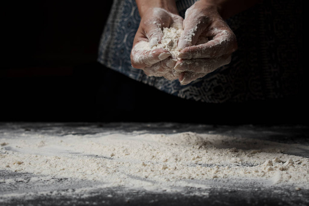 cropped shot of woman sifting wheat flour and making dough on black background - Zdjęcie, obraz