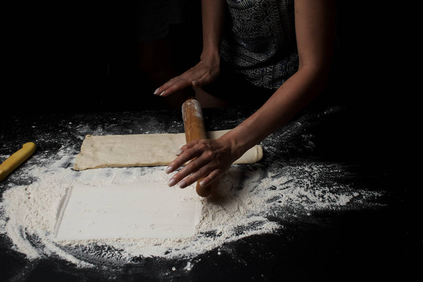 partial view of woman with rolling pin preparing dough on black surface - Foto, Bild