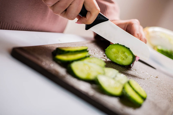 cropped shot of woman chopping fresh cucumber for healthy salad   - Фото, изображение
