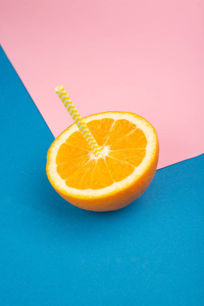 Nahaufnahme von aufgeschnittenen Orangen mit Stroh auf blauem und rosa Hintergrund - Foto, Bild