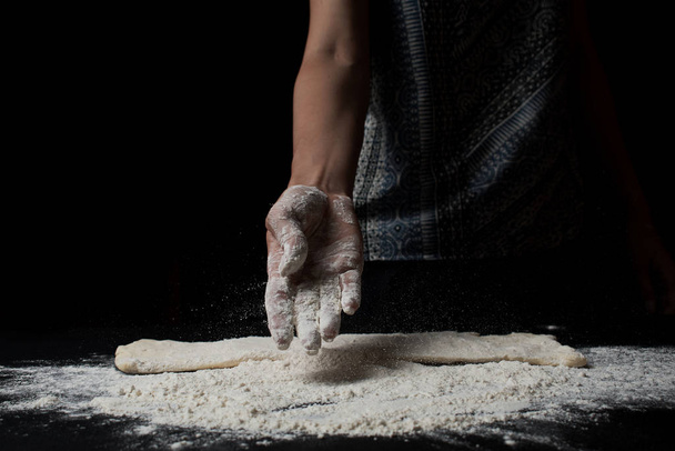 close-up partial view of woman sifting flour and cooking fresh homemade dough on black background - Fotó, kép