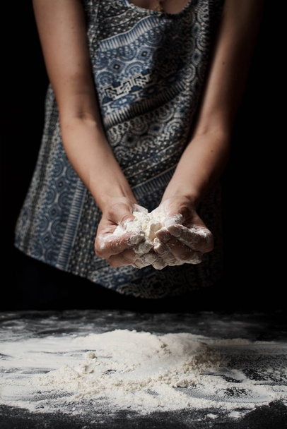 partial view of woman sifting flour and preparing dough on black background - Zdjęcie, obraz