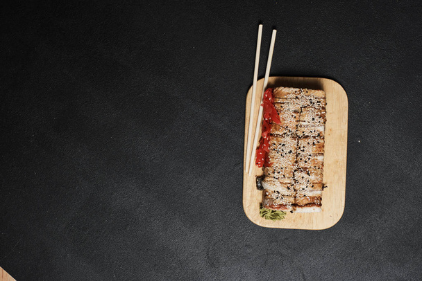 close-up view of sushi rolls and chopsticks on wooden board on black background   - Фото, зображення