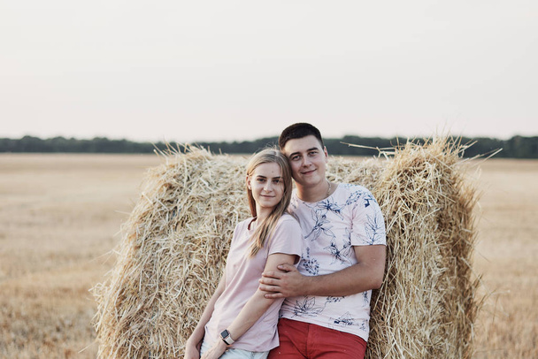 Schönes glückliches junges Paar in der Nähe von Heuballen auf dem Feld während der Ernte - Foto, Bild