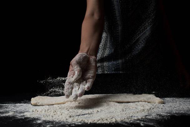 close-up partial view of woman sifting flour and cooking fresh homemade dough on black background - 写真・画像