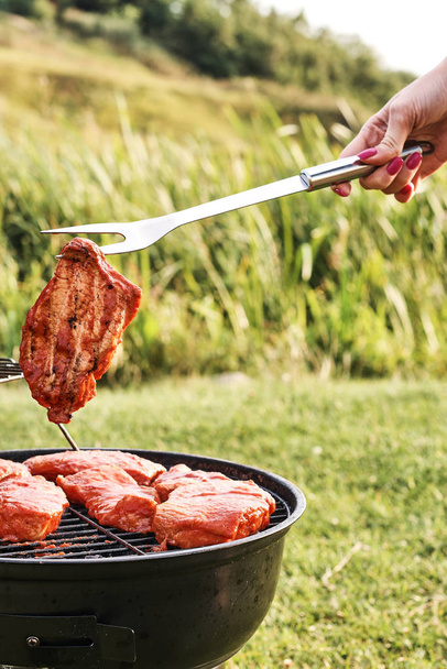 bijgesneden schot van vrouw koken vlees op houtskool grill buiten - Foto, afbeelding