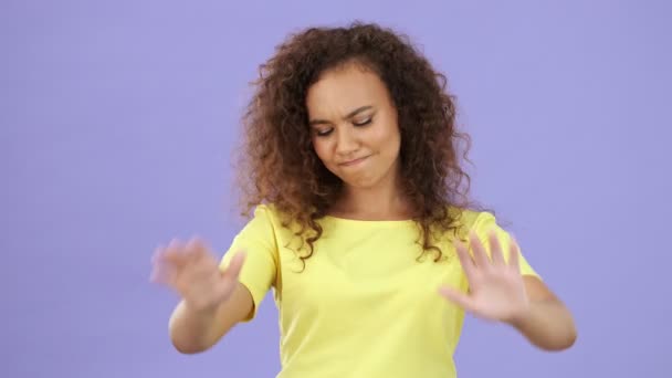 Beautiful african young woman in yellow t-shirt crossing her arms and showing no sign with hands while looking at the camera over purple background isolated - Metraje, vídeo