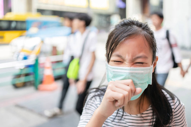 Asijské dítě dívka trpí kašel s obličejovou maskou, nemocná žena dospívající nosit lékařskou masku z důvodu znečištění ovzduší ve městě ulici, prach mouchy ve vzduchu, koncept znečištění, prachové alergie - Fotografie, Obrázek