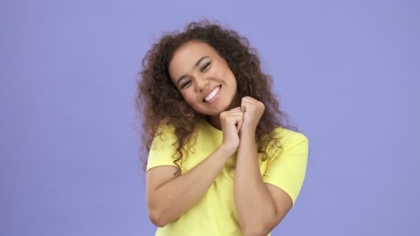 Attractive happy african young woman in yellow t-shirt enjoying of something over purple background isolated - Video