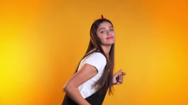 Pretty young girl in dress smiling and dancing in excellent mood on yellow background. Happiness, party concept. - Video