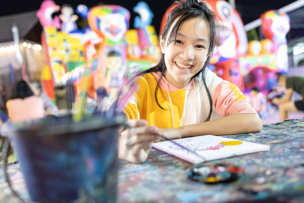 幸せなアジアの子供の女の子は、絵を描くためにパレットや絵筆で水彩を使用して楽しい、夜にリラックスした笑顔の女性を持つペイント活動を楽しむ、研究、芸術を学ぶ、コンセプト開発、趣味、活動  - 写真・画像