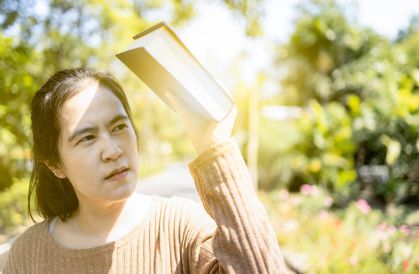 Mujer asiática sostiene un libro que cubre el sol para prevenir la piel facial
  - Foto, Imagen