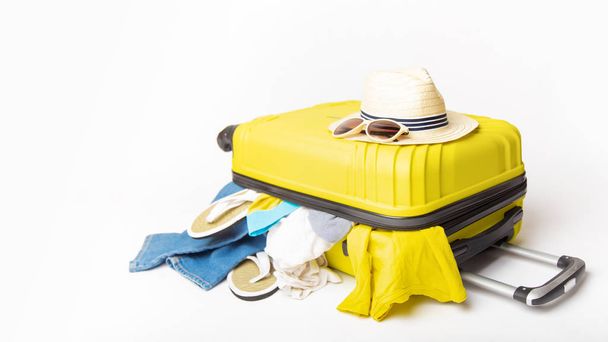 hat and sunglasses on a yellow suitcase with clothes of the traveler on a white background. Travel and adventure concept - Φωτογραφία, εικόνα