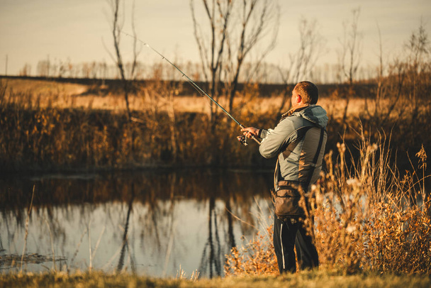 Um pescador homem pescando no rio com uma vara de pesca
. - Foto, Imagem