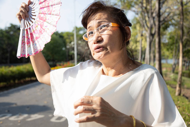 Aasian vanhempi nainen fanning ja hiki kasvot kärsivät auringonpolttama erittäin kuuma kesällä sää ongelma tuntuu heikko, väsynyt nainen vanhukset lämpöhalvaus kadulla, korkea lämpötila aurinkoisena päivänä
 - Valokuva, kuva