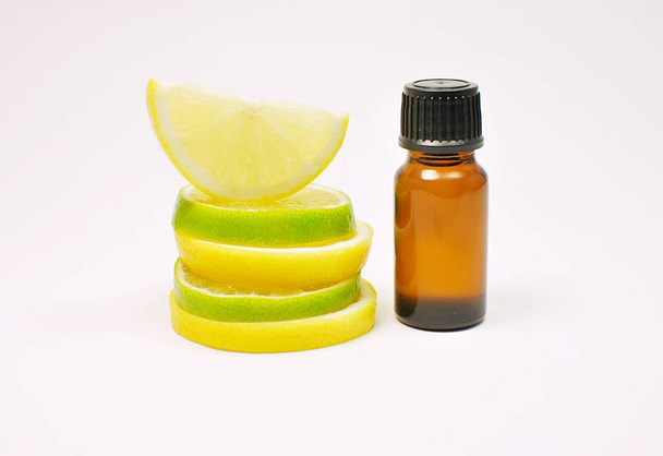 Aceite esencial de cítricos, maqueta botella marrón, rodajas de limón y lima aisladas sobre fondo blanco
. - Foto, imagen