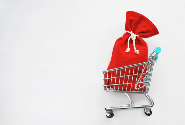 Compras de Navidad, concepto de venta. Bolso de Santa Claus rojo en el carrito de compras sobre fondo blanco
. - Foto, Imagen