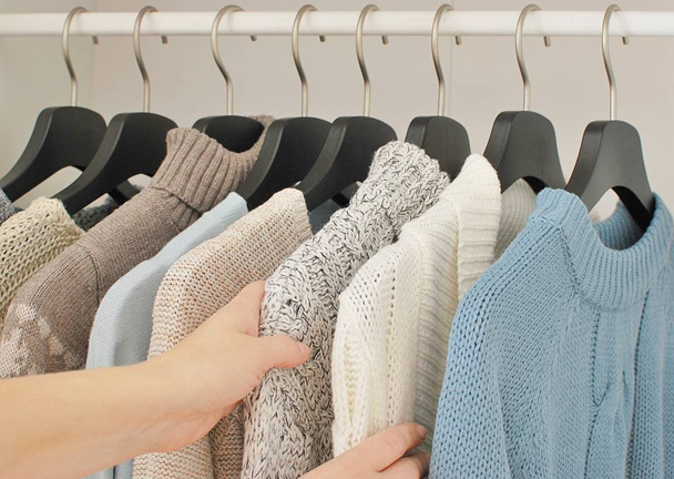 Herbst - Winter Mode Konzept. Frau wählt warme Stricksachen auf Kleiderbügeln im Kleiderschrank. - Foto, Bild